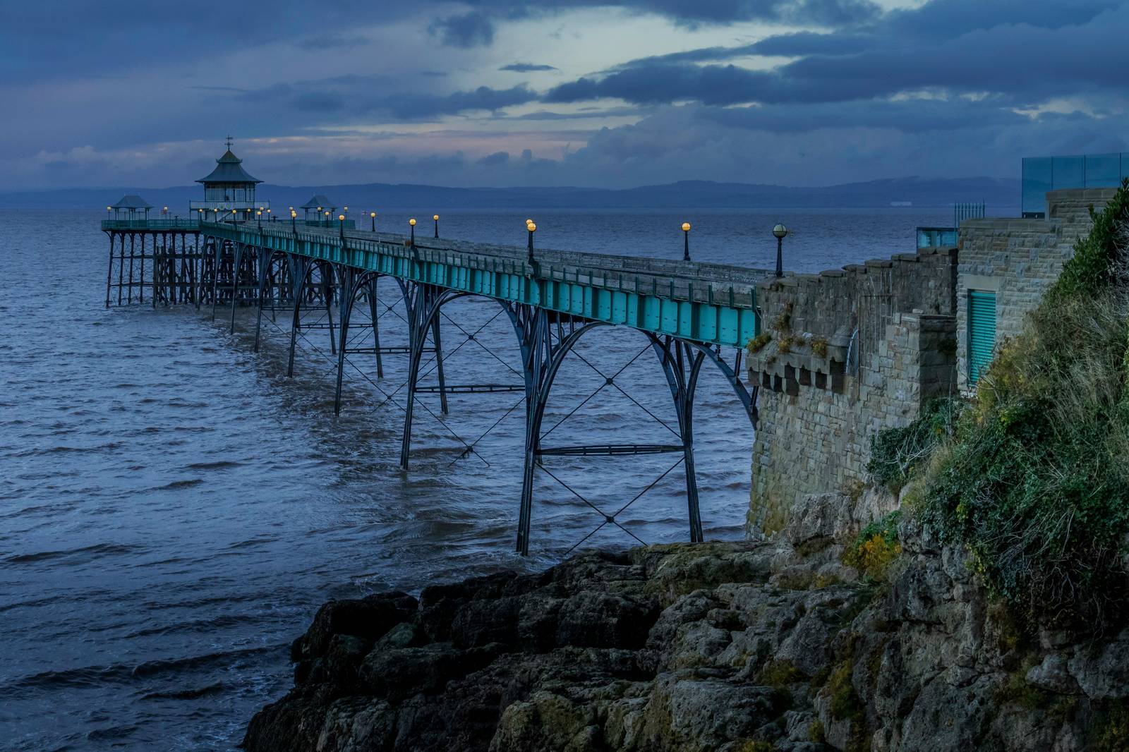 A Victorian pier with teal ironwork stretching into the sea at dusk